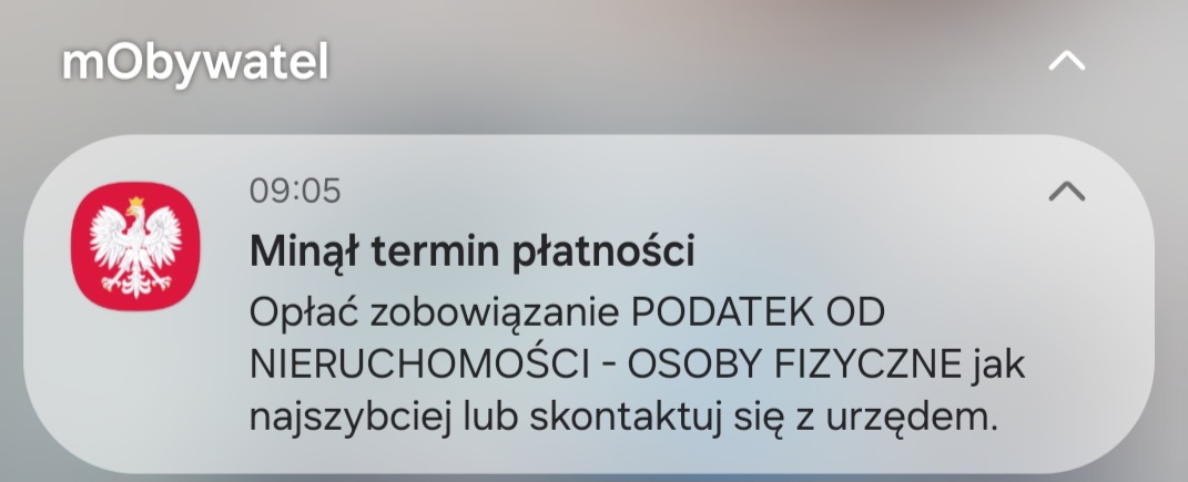 Grafika przedstawia powiadomienie systemowe z&nbsp;aplikacji mObywatel wyświetlone na&nbsp;ekranie smartfona. Tekst powiadomienia brzmi: &bdquo;Minął termin płatności. Opłać zobowiązanie PODATEK OD NIERUCHOMOŚCI - OSOBY FIZYCZNE jak najszybciej lub&nbsp;skontaktuj się z&nbsp;urzędem&rdquo;. Obok tekstu widnieje godzina 09:05 oraz&nbsp;godło Polski na&nbsp;czerwonym tle.
