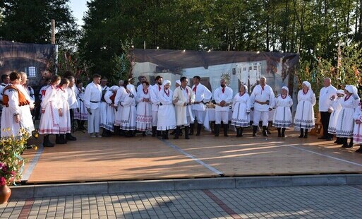 zdjęcie z końcowej części widowiska łętowskei wesele z liczną grupa aktorów na scenie przyozdobionej wiesjkimi dekoracjam i weselna scenografiąi