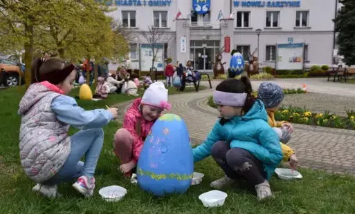 zdjęcie przedstawia trzech przedszkolaków malujących jajo wielkanocne przed budynkiem Urzędu Miasta i Gminy w Nowej Sarzynie