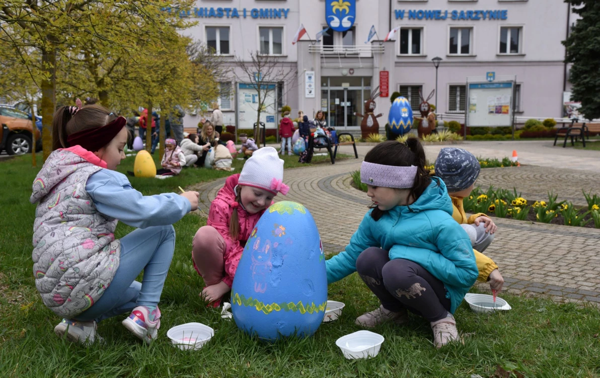 zdjęcie przedstawia trzech przedszkolaków malujących jajo wielkanocne przed budynkiem Urzędu Miasta i Gminy w Nowej Sarzynie