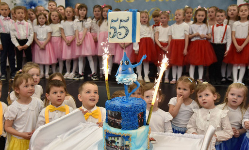 tort z okazji 55-lecia przedszkola, w tle dzieci uczestniczące w uroczystości jubileuszowej